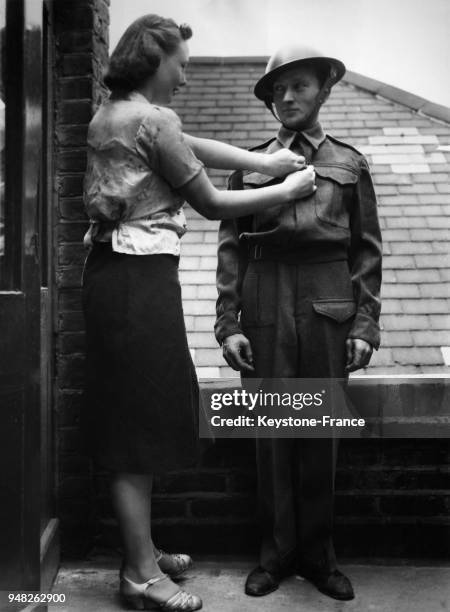 Une jeune femme à la porte d'une usine reboutonne la veste militaire d'une jeune recrue, à Londres, Royaume-Uni circa 1930.