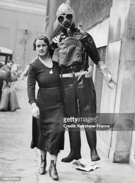 Une femme pose aux côtés d'un homme vêtu d'une combinaison de protection et muni d'un masque à gaz, à Londres, Royaume-Uni en mars 1937.