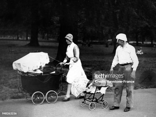 Un père promène son enfant dans la poussette tandis qu'une nurse promène le bébé dans son landau, à Hyde Park à Londres, Royaume-Uni circa 1930.