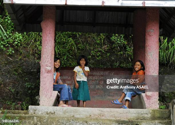 Philippines, Banaue, three girls under a structure sitting by pillars and smiling.