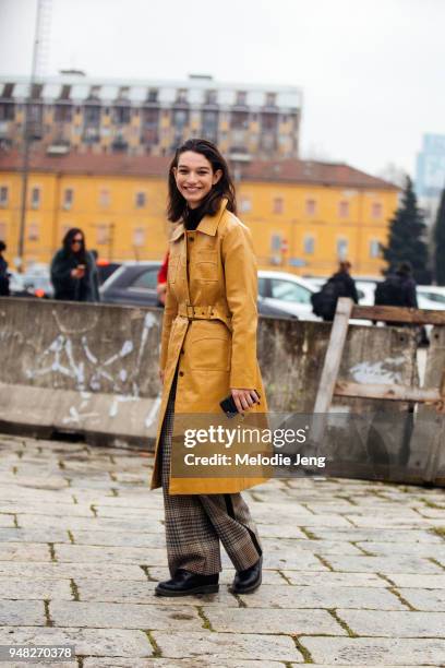 Model Mckenna Hellam wears an amber leather coat pockets and a belt, plaid trousers, and black boots during Milan Fashion Week Fall/Winter 2018/19 on...