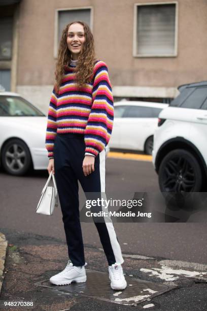 Polish model Michelle Gutknecht wears a white, pink, and blue striped sweater, blue runner pants with a white stripe, a white purse, and white chunky...