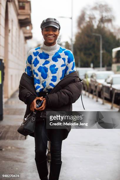 Nigerian model Mayowa Nicholas wears a black newsboy cap, hoop earrings, a gray and blue sweater, and her black jacket around off her shoulders...