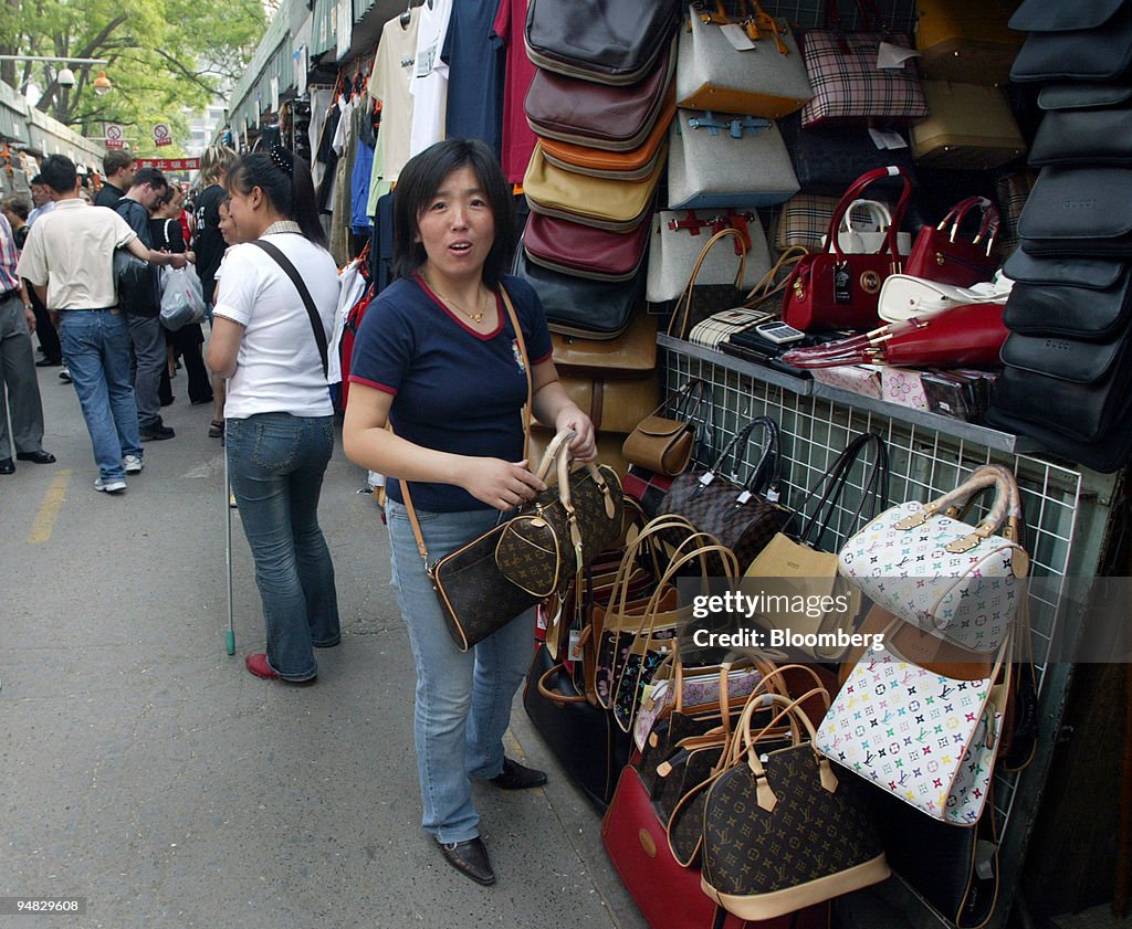 A vendor arranges fake Louis Vuitton handbags at a street stall in