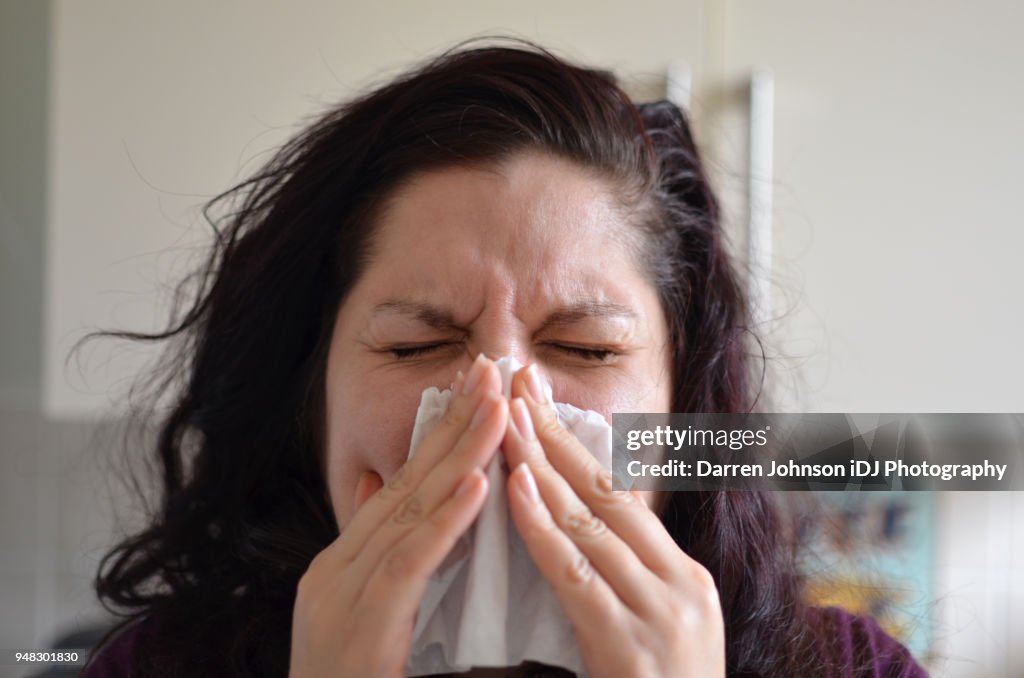 Woman blowing her nose hard into a tissue at home