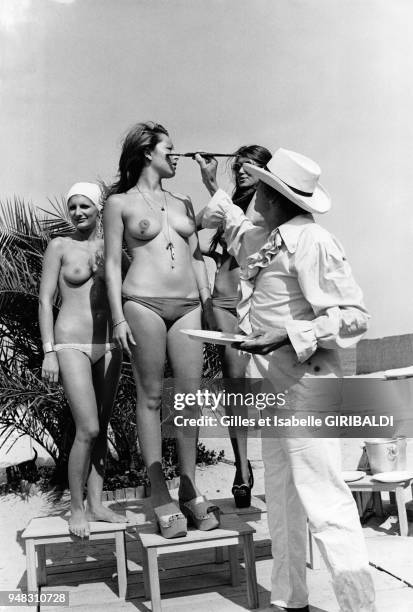 Artiste Yves Corbassière peint sur le corps d'une jeune femme en monokini sur la plage de Pampelonne pendant que deux autres attendent leur tour,...