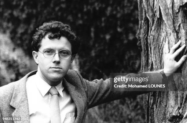 écrivain Pascal Ory pose la main appuyée sur un tronc d'arbre dans un jardin à Paris, France, en mars 1985.