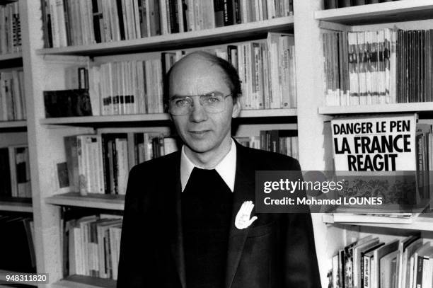 évêque d'Evreux, Mgr Gaillot, posant devant une bibliothèque sur laquelle est posé un livre 'Danger le Pen-La France réagit' et portant un badge...