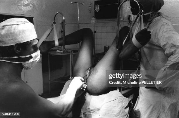 Un homme avec masque et gants et son assistante en train d'exciser une jeune mariée, sur la table gynécologique, les pieds dans les étriers, à...