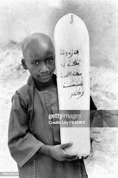 Enfant présentant une tablette coranique, servant à l'apprissage de la lecture par les versets du Coran, à Djenné, au Mali, en 1987.