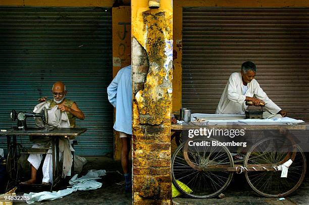 Customer gets changed behind the scant cover of a brick column between two elderly tailors on a sidewalk in Sikanderpur, India April 30, 2004.