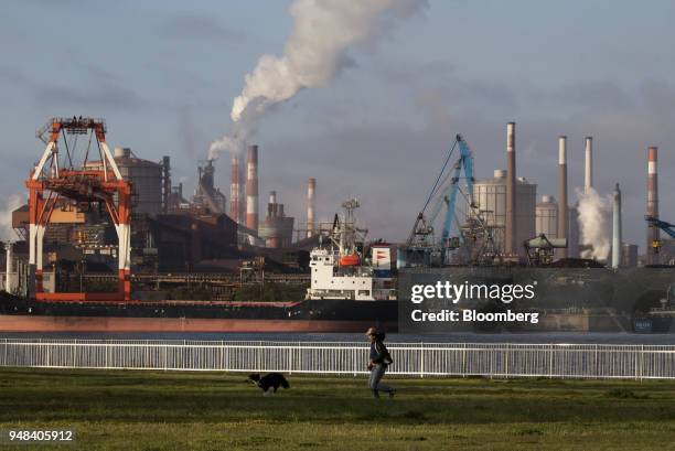 Man runs with a dog in front of the Nippon Steel & Sumitomo Metal Corp. Plant at a park in Kamisu, Ibaraki, Japan, on Wednesday, April 18, 2018....