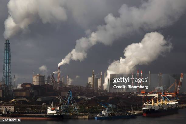 Emissions rise from chimneys as bulk carrier ships sit moored at the Nippon Steel & Sumitomo Metal Corp. Plant in Kashima, Ibaraki, Japan, on...