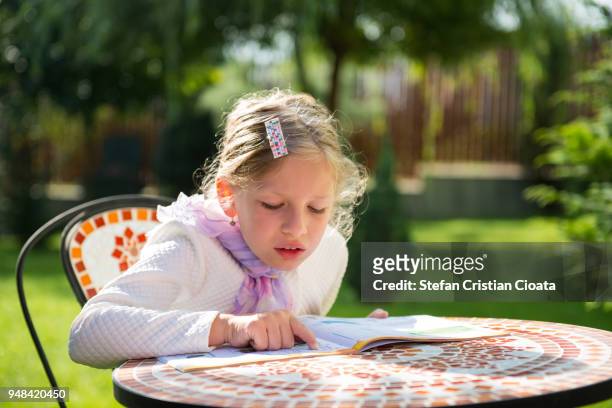 girl reading at table in backyard - fille lire gazon photos et images de collection