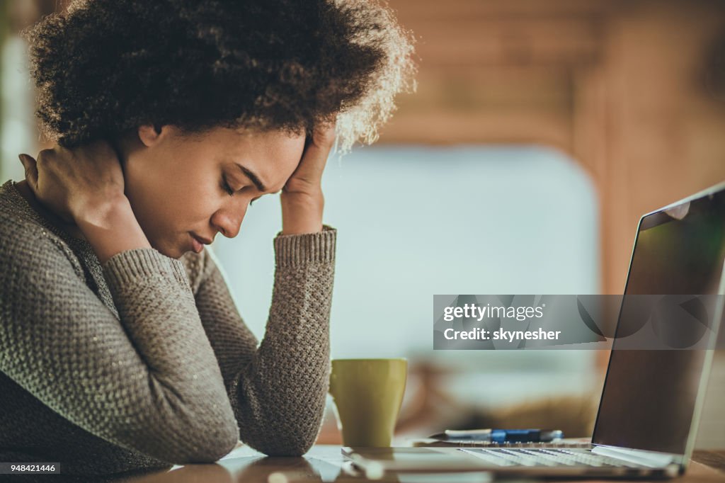 Afrikanische amerikanische Frau, die Kopfschmerzen von der Arbeit an einem Computer zu Hause.
