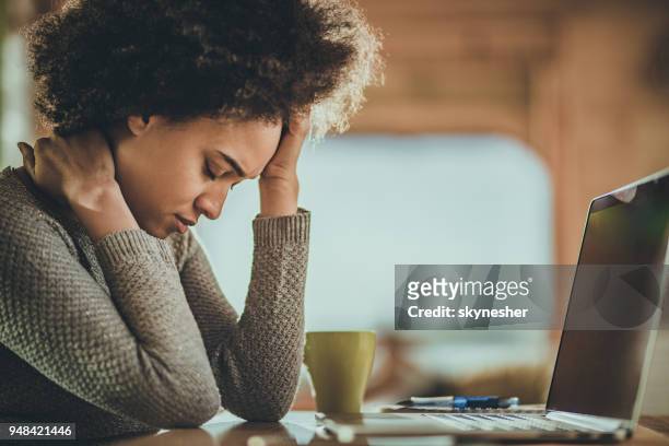 african american vrouw met een hoofdpijn van het werken op een computer thuis. - wallen stockfoto's en -beelden