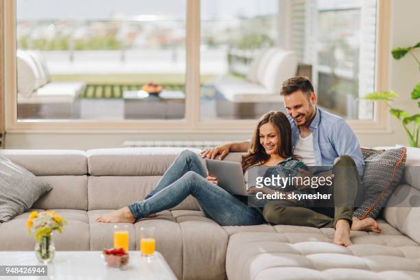 happy couple in love surfing the internet on laptop at home. - young couple on couch stock pictures, royalty-free photos & images