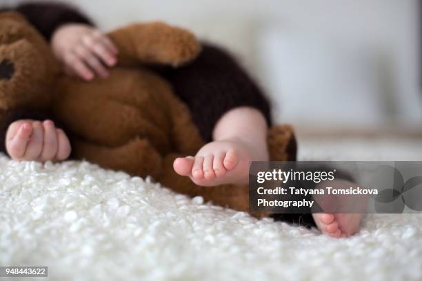 sweet little baby boy, dressed in handmade knitted brown soft teddy bear overall, sleeping cozy at home in sunny bedroom with lots of teddy bears around him - baby stuffed animal bildbanksfoton och bilder