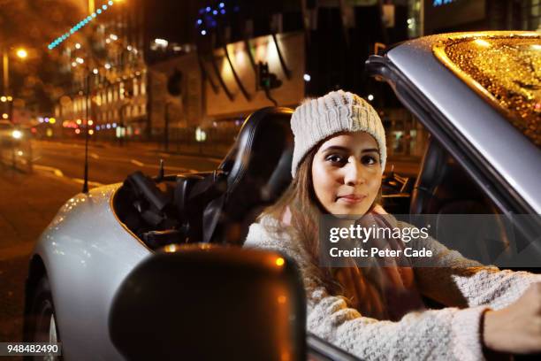 young woman driving car through city at night - convertible top stock pictures, royalty-free photos & images