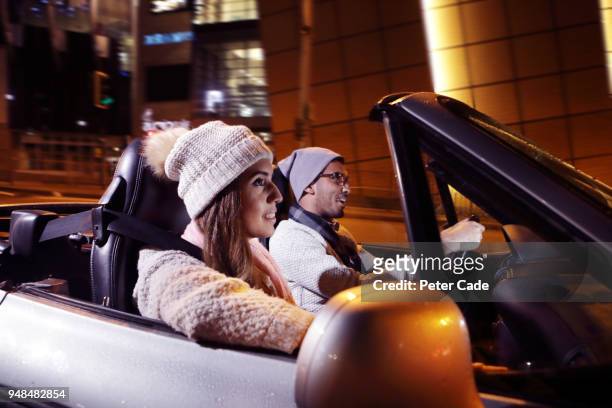 young couple driving car through city at night - convertible top stock pictures, royalty-free photos & images