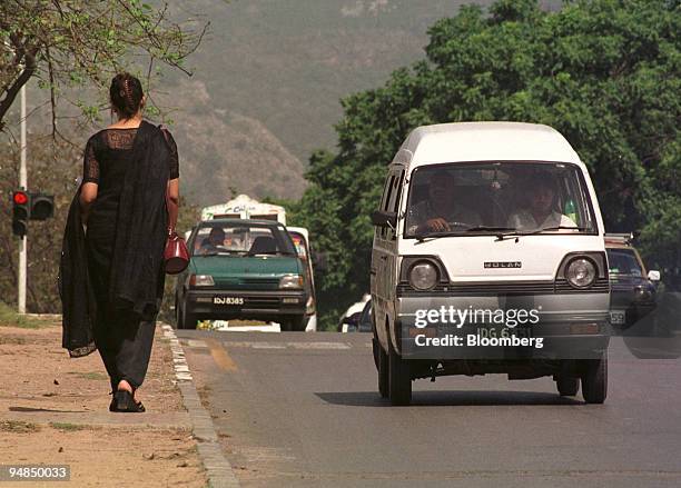 Traffic passes a woman as she walks down a street in Islamabad, Pakistan on April 9, 2004. Shares of Pak Suzuki Motor Co. And Indus Motor Co.,...