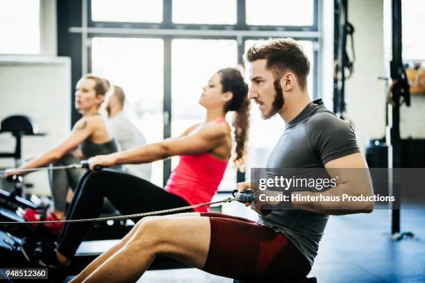 people using rowing machines at gym - gym equipment red stock pictures, royalty-free photos & images