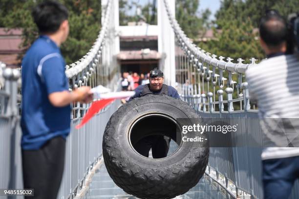 This picture taken on April 18, 2018 shows a competitor taking part in a tyre flipping competition on a glass-bottomed bridge in Pingjiang in China's...