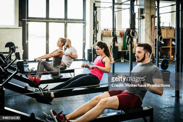 fitness enthusiasts exercising using rowing machines - gym ストックフォトと画像