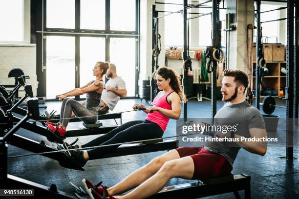 fitness enthusiasts exercising using rowing machines - gym imagens e fotografias de stock
