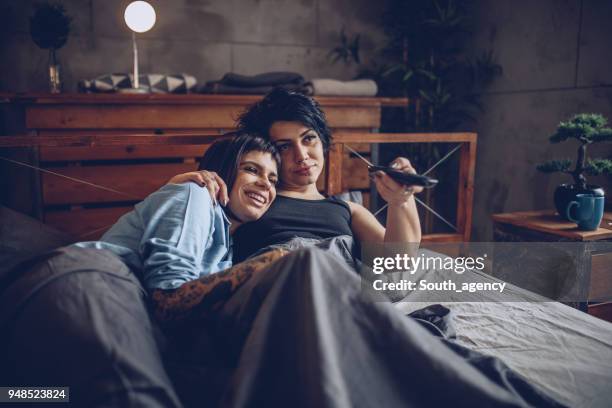 unga lesbisk par titta på tv i sängen - couple tv bildbanksfoton och bilder