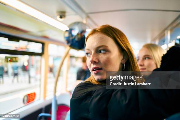 redhead teenager travelling with a group of friends on the bus, holding on to the handrail and looking out of the window at something or someone or thinking or contemplating - hauptverkehrszeit stock-fotos und bilder
