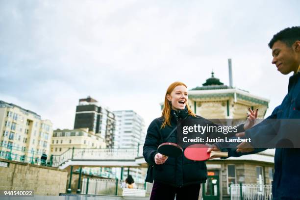 teenage boyfriend and girlfriend playing table tennis on the beach in winter having fun and joking smiling together - friends table tennis stock pictures, royalty-free photos & images