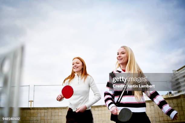 two teenage girls with long hair, one blonde one redhead playing doubles table tennis with friends, laughing and smiling in the winter - friends table tennis stock pictures, royalty-free photos & images