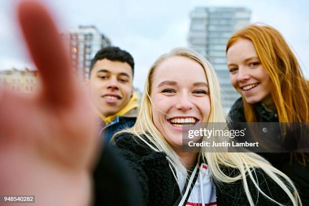 three teenagers taking a selfie on their mobile phone taken from the phone's perspective with hand in view of the camera. two friends lean in from both sides smiling at camera - adolescents selfie ストックフォトと画像