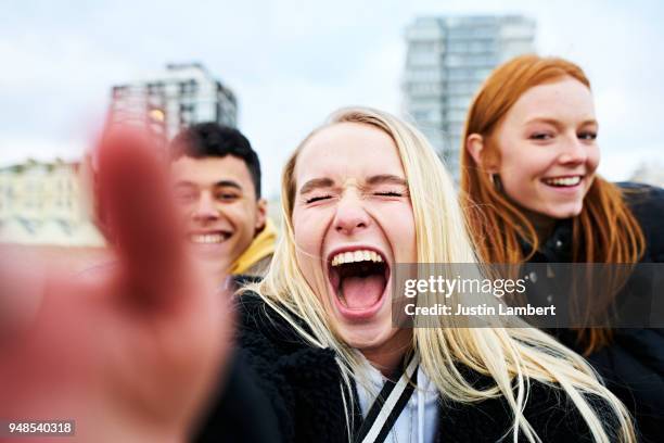 three teenagers taking a selfie on their mobile phone taken from the phone's perspective with hand in view of the camera. two friends lean in from both sides with main woman smiling and laughing openly while the picture is taken, all smiling at camera - adolescents selfie ストックフォトと画像