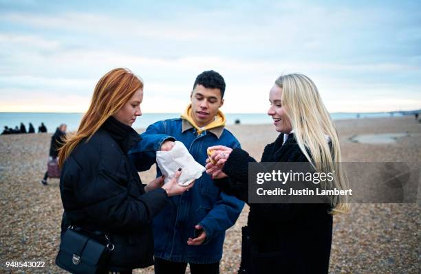 three friends sharing a donut on the beach in winter - friends donut stock-fotos und bilder