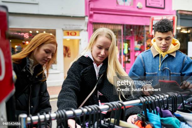 three teenage friends looking at second hand clothes outside a vintage clothes store - shopaholic stock pictures, royalty-free photos & images