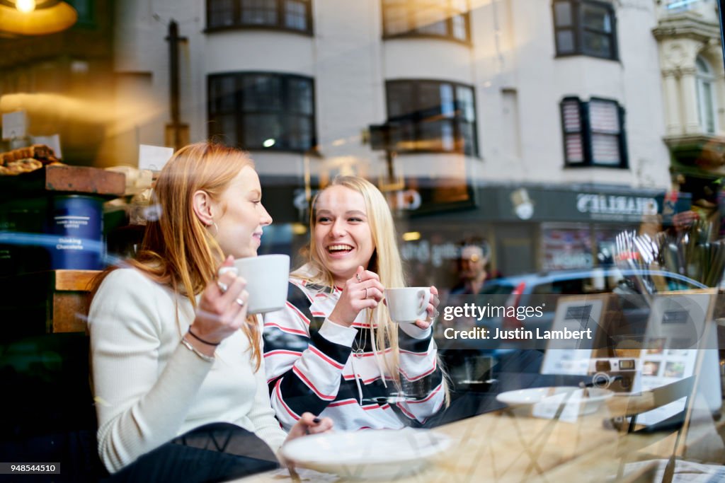 Two teenage female friends enjoying a coffee and a moment together sitting in a cafe window