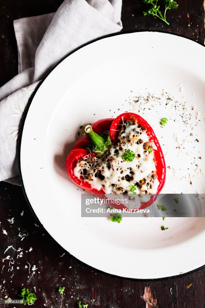 Top view of baked in the oven red bell pepper stuffed with minced pork and beef meat, covered with melted cheese, served with fresh parsley in a plate on a wooden table. Comfort food. Picnic food.