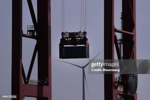 Crane lifts a shipping container as a wind turbine stands beyond at Terminal Burchardkai in the Port of Hamburg in Hamburg, Germany, on Wednesday,...