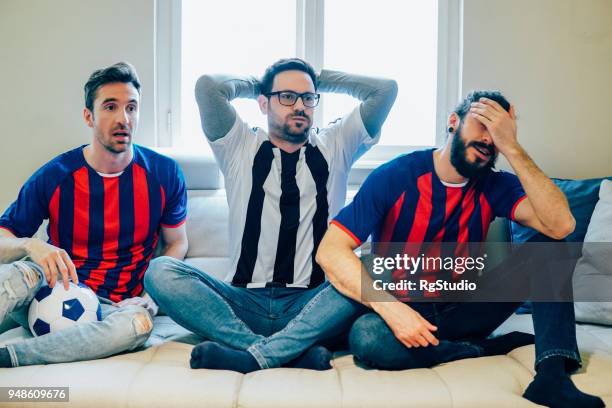 three disappointed men watching football game wearing sports jerseys - match 3 stock pictures, royalty-free photos & images