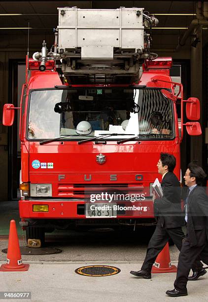 Two Japanese businessmen walk past a Mitsubishi Fuso-built fire truck parked at a fire station in downtown Tokyo on Wednesday, December 22, 2004....