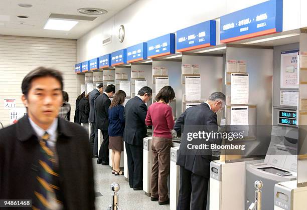 Man, left, walks out of a Mizuho Bank branch in downtown Tokyo while other customers use ATMs on Monday, December 20, 2004. Mizuho Financial Group...