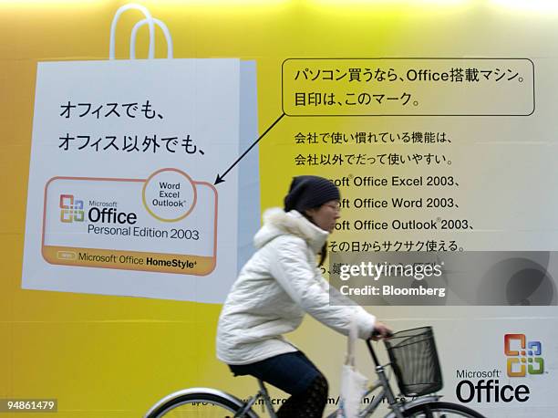 Woman rides a bicycle by a billboard advertising Microsoft Office Homestyle outside an electronics store in downtown Tokyo on Monday, December 20,...