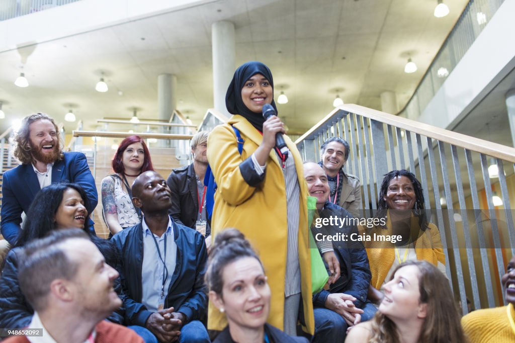 Smiling woman in hijab speaking with microphone in conference audience