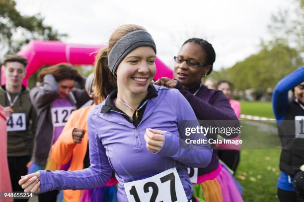 woman pinning marathon bib on friend at charity run in park - bib stock pictures, royalty-free photos & images