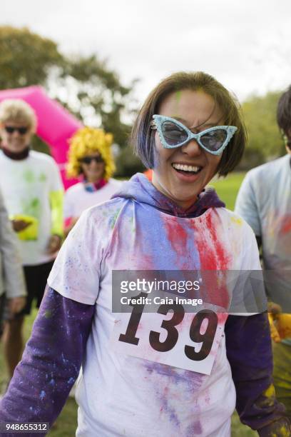 portrait playful female runner in sunglasses and holi powder at charity run in park - holirun stock-fotos und bilder