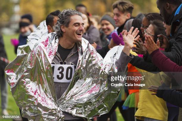 enthusiastic male marathon runner in thermal blanket high-fiving spectators - marathon zuschauer stock-fotos und bilder