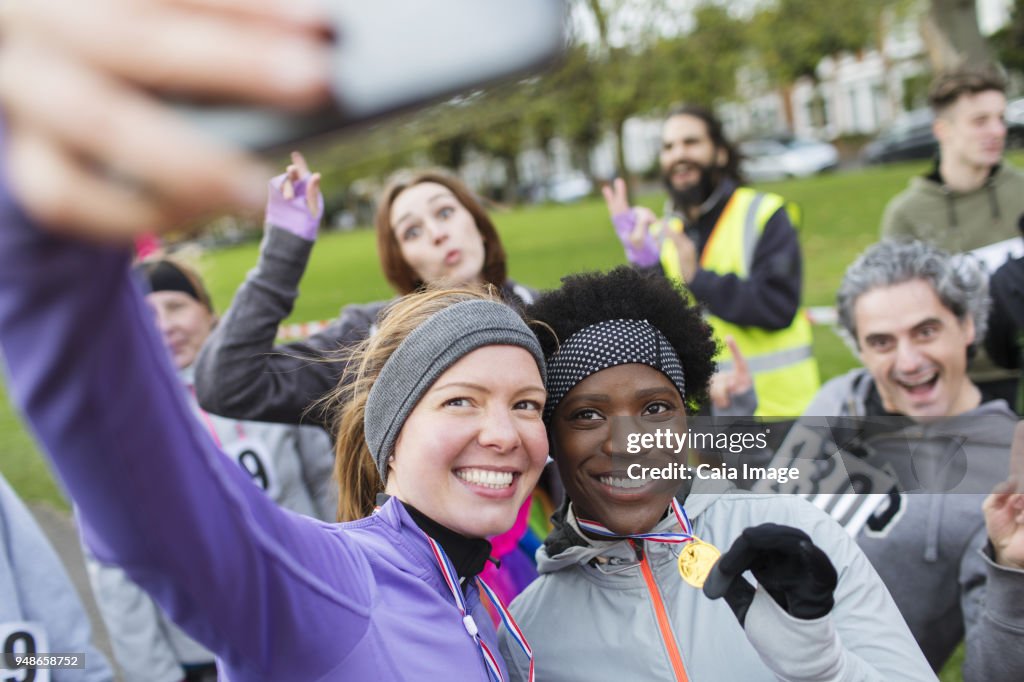 Smiling female runners with medal taking selfie at charity run in park