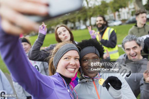 smiling female runners with medal taking selfie at charity run in park - comedy honors awards show stock pictures, royalty-free photos & images